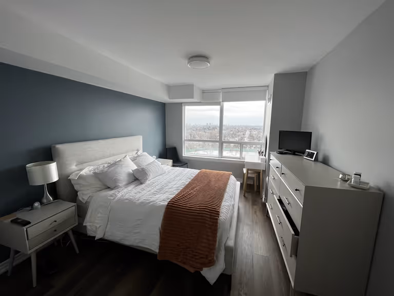 A bedroom showcasing a bed, dresser, and a captivating city view, offering a serene and stylish living space.