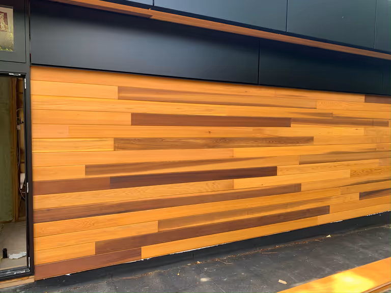A wooden wall with a black door and a bench, creating a rustic ambiance.